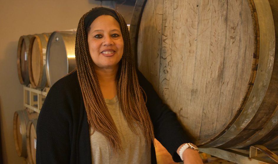 Donna Stoney stands smiling in front of a large wooden wine barrel