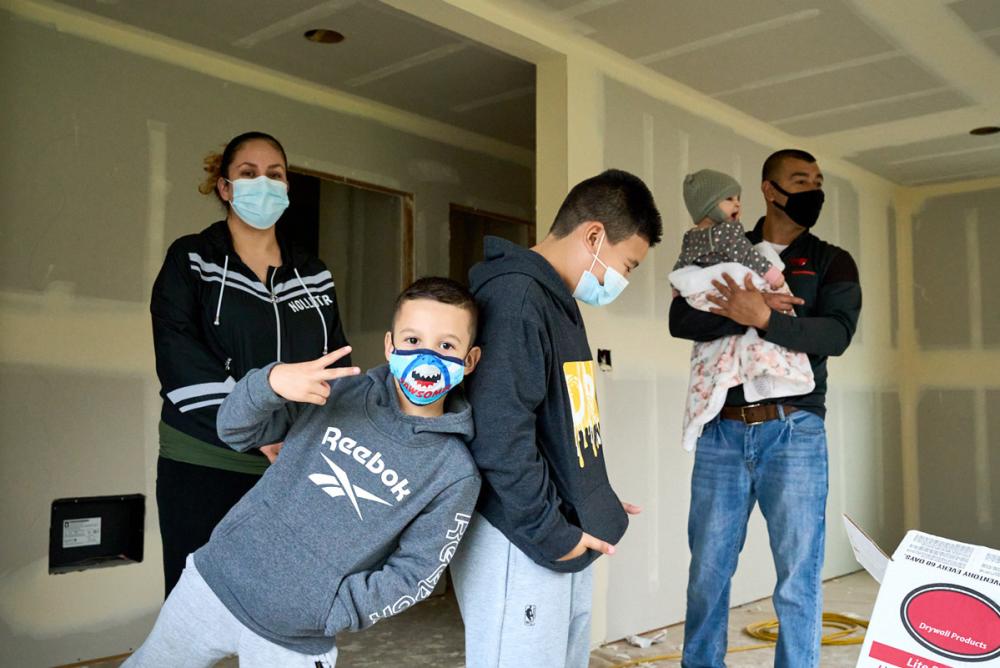 A family of two parents and three kids stands inside a house under construction