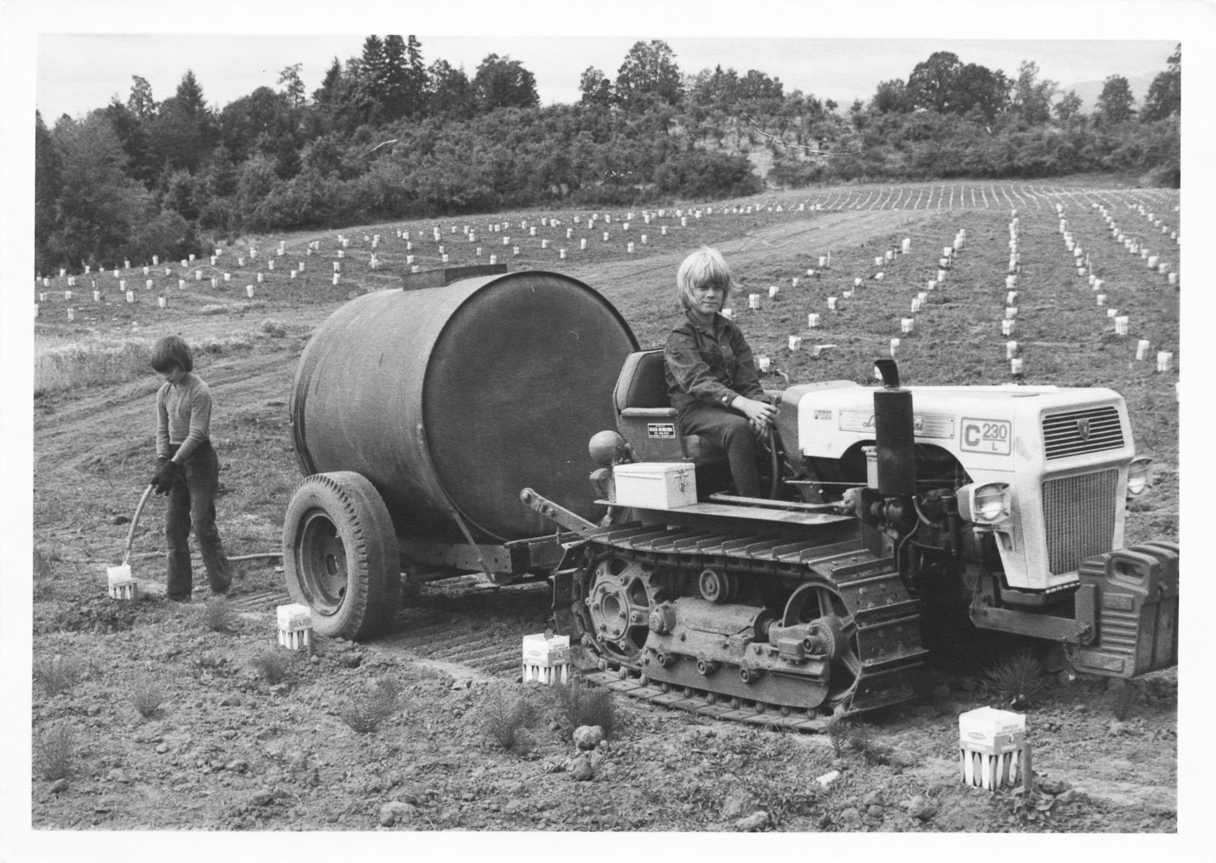 black and white photo of children on a tractor watering small grapevines