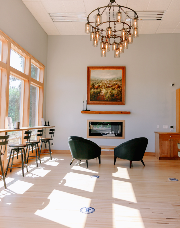 Tasting Room Interior, Large chandelier hanging over two plush chairs facing an indoor fireplace