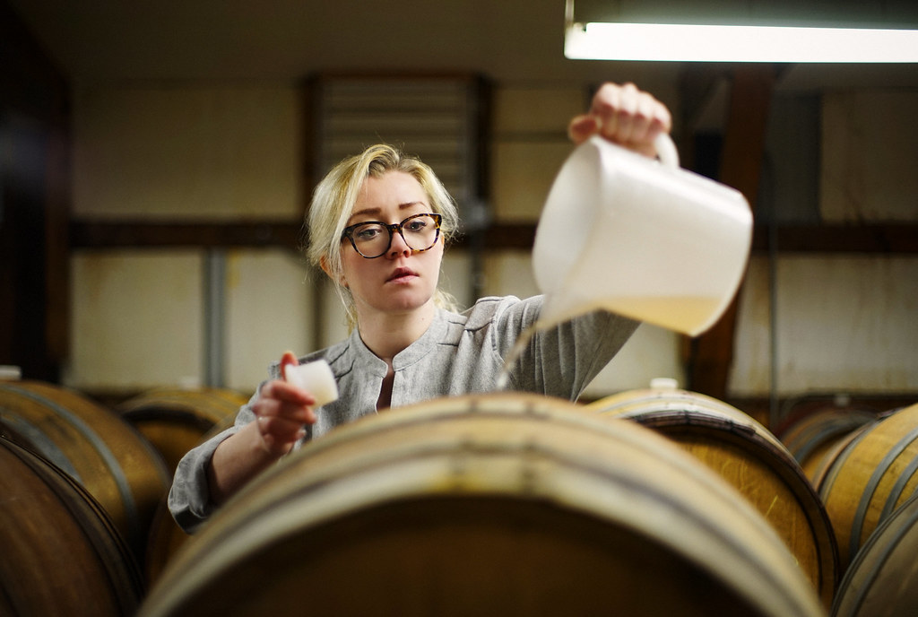 A woman pours wine from a plastic jug into a large wooden barrel